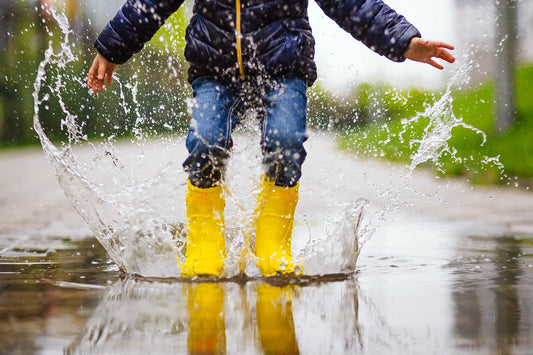 child playing in puddle with yellow gumboots on