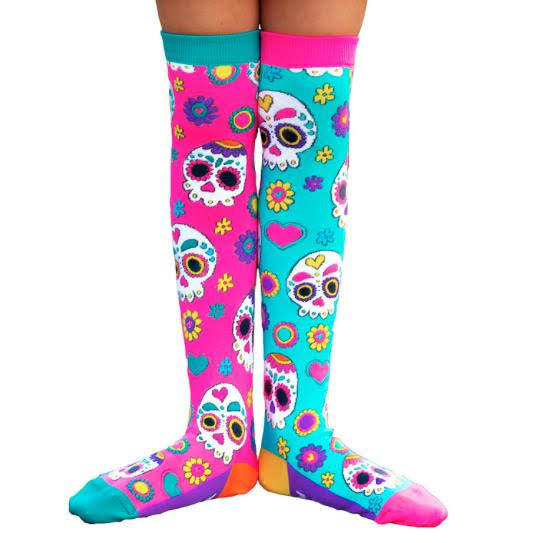 A pair of colorful knee-high socks featuring sugar skull designs, pink on the top, blue in the middle, and yellow at the bottom, with various patterns including flowers and hearts.