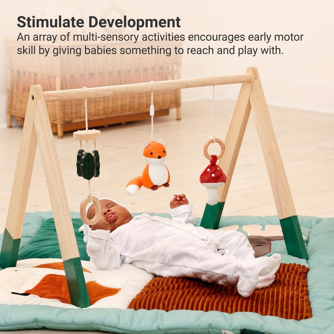 Baby lying on a play mat with a wooden baby gym and hanging toys in a nursery.