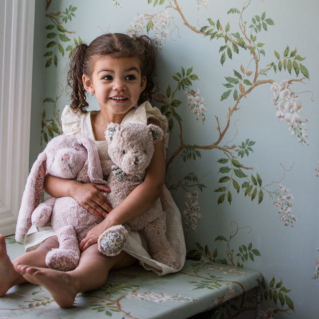 Child holding teddy bears in a room with floral wallpaper