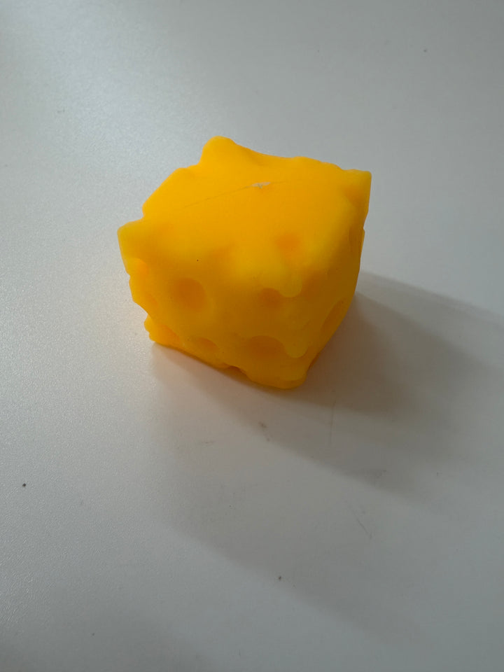 A novelty yellow candle shaped like a Swiss cheese cube, sitting on a plain light gray surface.