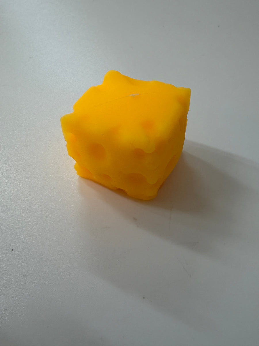 A novelty yellow candle shaped like a Swiss cheese cube, sitting on a plain light gray surface.