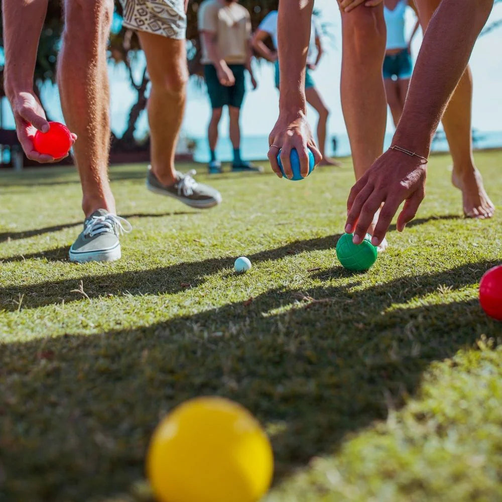 People playing bocce ball on a grassy outdoor area with colorful balls.