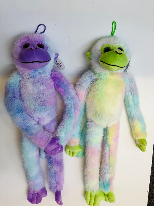Two plush monkey toys with pastel tie-dye fur hanging against a plain white background. One monkey is purple and blue, and the other is green and yellow.