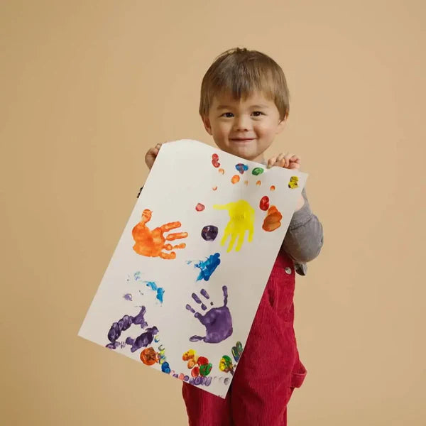 Child holding a sheet of paper with colorful handprints against a beige background using honeysticks
