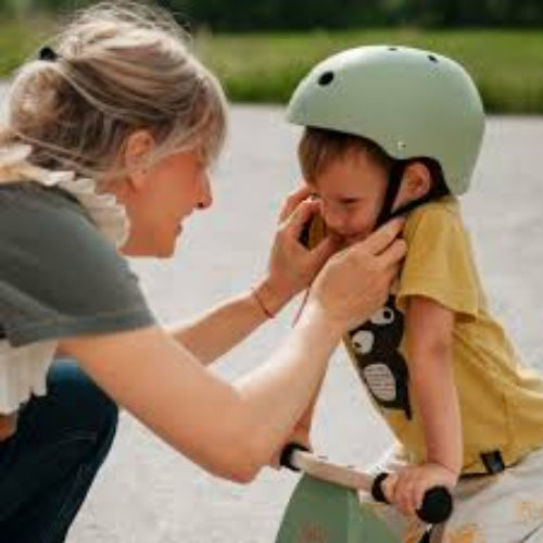Woman adjusting a child's helmet while standing on a paved path