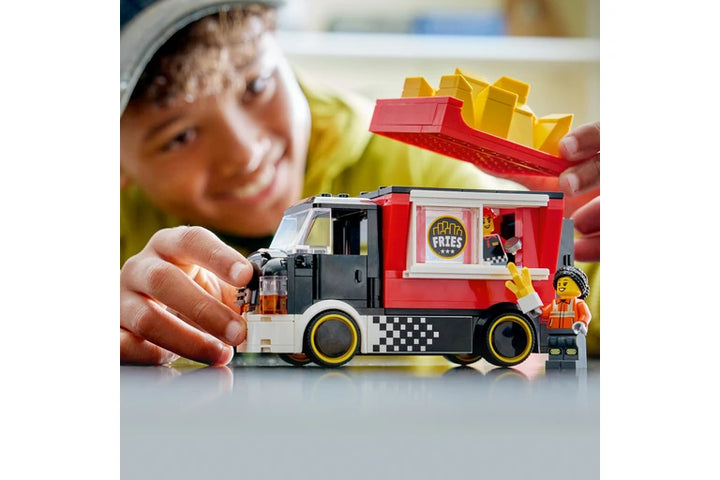Child playing with a lego food truck model, likely made of building blocks, on a white surface.