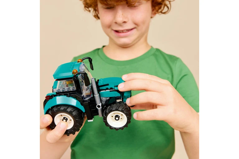 A child wearing a green t-shirt holds a lego toy tractor against a plain beige background.