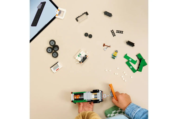 Top-down view of a child's hands assembling a small green and white toy vehicle with wheels and accessories scattered on a beige tabletop.