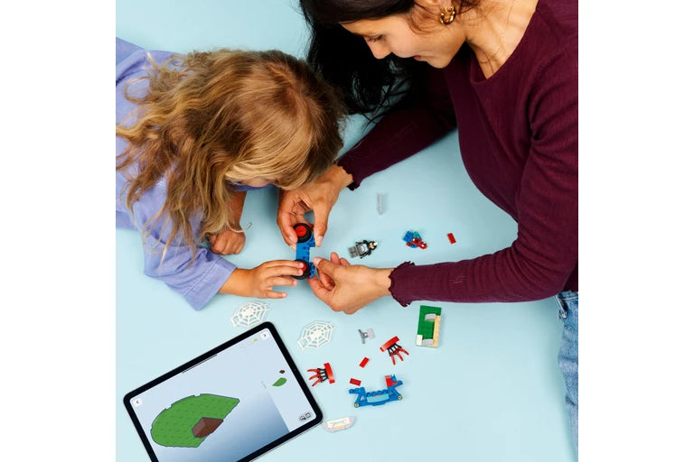 Woman and child playing with lego figures on a light blue surface, with a tablet showing a map.