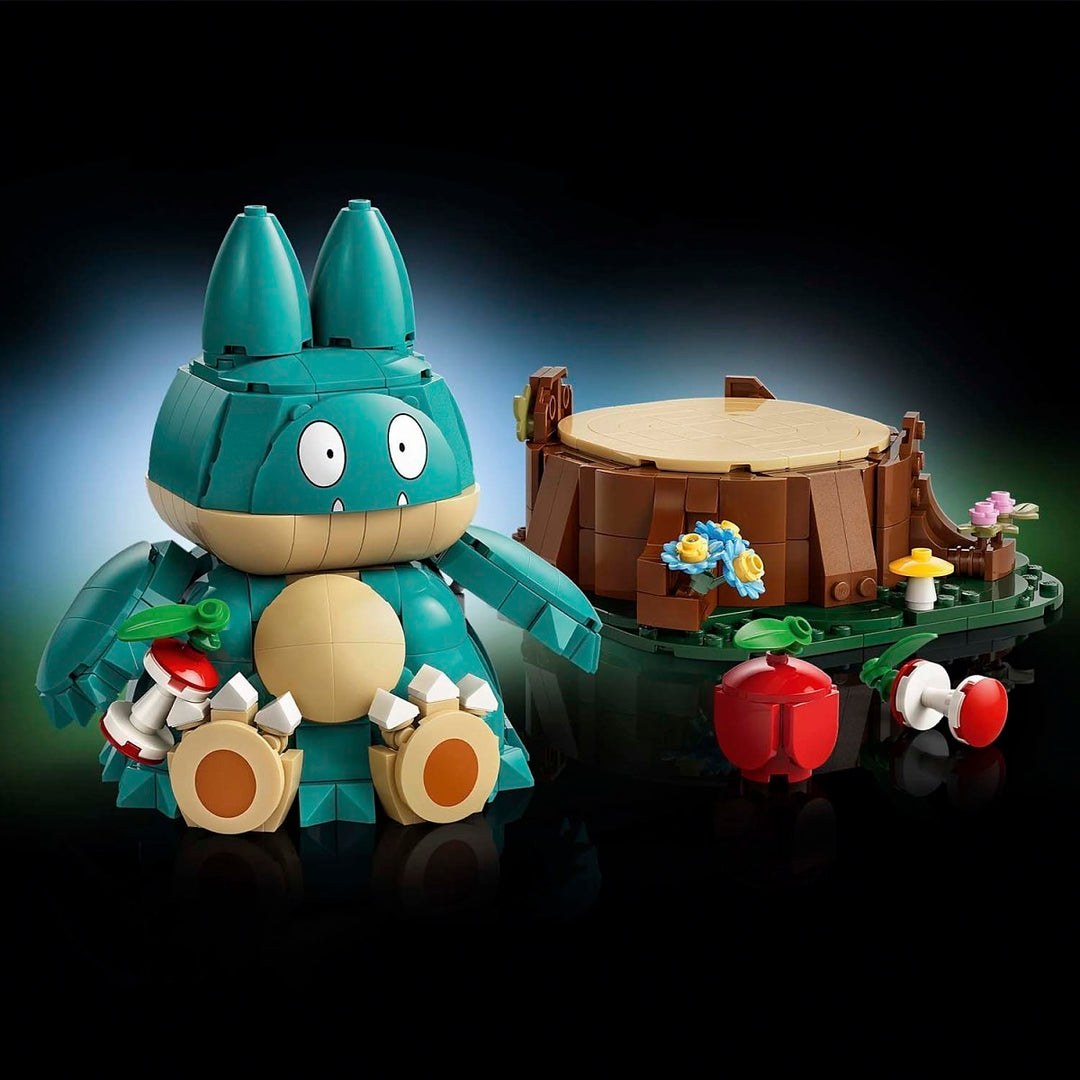 A toy building-block set featuring a teal and beige rabbit-like character figure beside a small treehouse with flowers, mushrooms, and red apple pieces, photographed on a dark studio background.