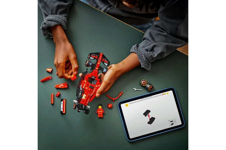 Person assembling a red and black toy robot on a green table with a tablet displaying instructions.