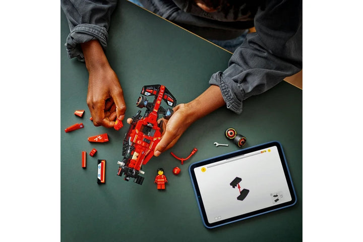 Person assembling a red and black toy robot on a green table with a tablet displaying instructions.