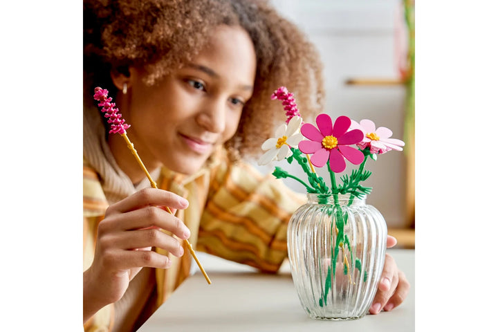 person holding a vase with pink lego flowers and a stick with a flower on a white background