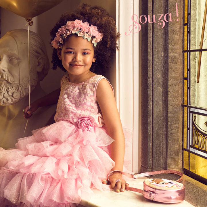 Young girl in a pink dress with a flower crown sitting next to a decorative suitcase.