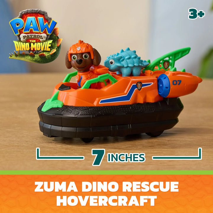 Paw Patrol Dino Rescue Hovercraft toy featuring Zuma in an orange hovercraft with a blue dinosaur passenger, shown on a wooden surface with size and branding text overlays.