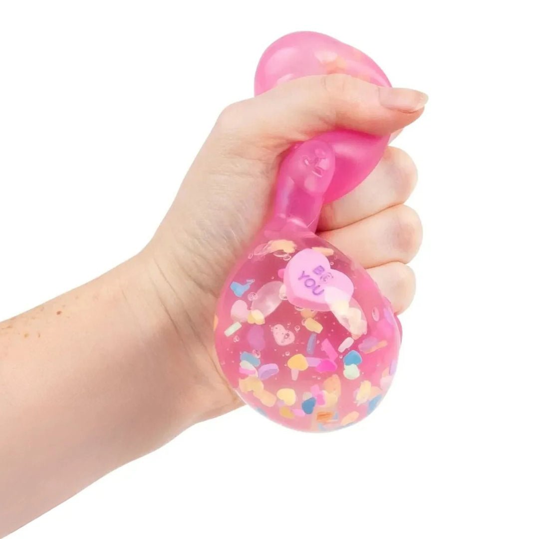 Hand holding a pink stress bear with colorful confetti and 'I love you' message on a white background