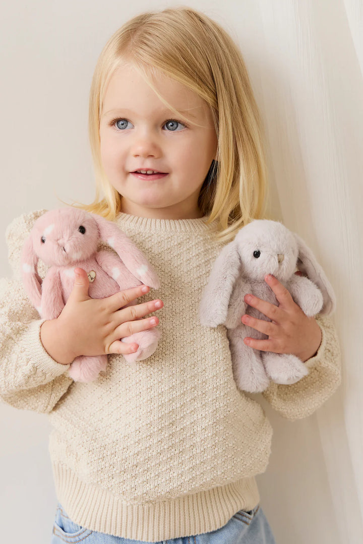 Child holding two stuffed animals against a plain background