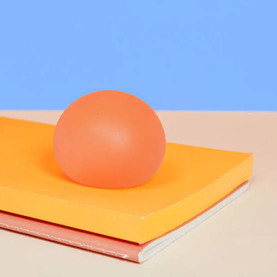 speks reef stress ball resting on top of stacked yellow and pink rectangular blocks against a blue and beige background.