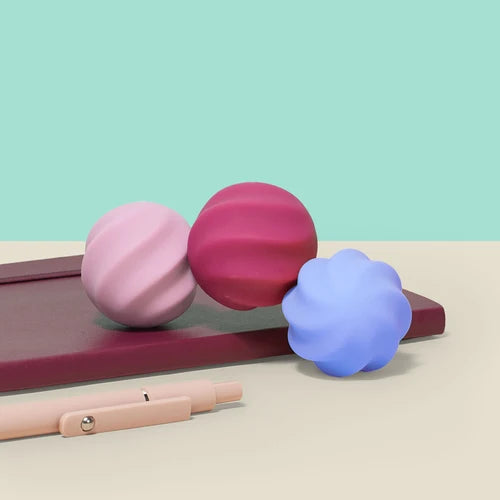 Three colorful Speks soft silicone fidget magnets Swirls on a pink stand with a light blue background