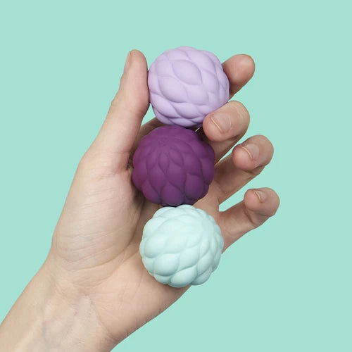 Hand holding three textured stress balls against a light green background