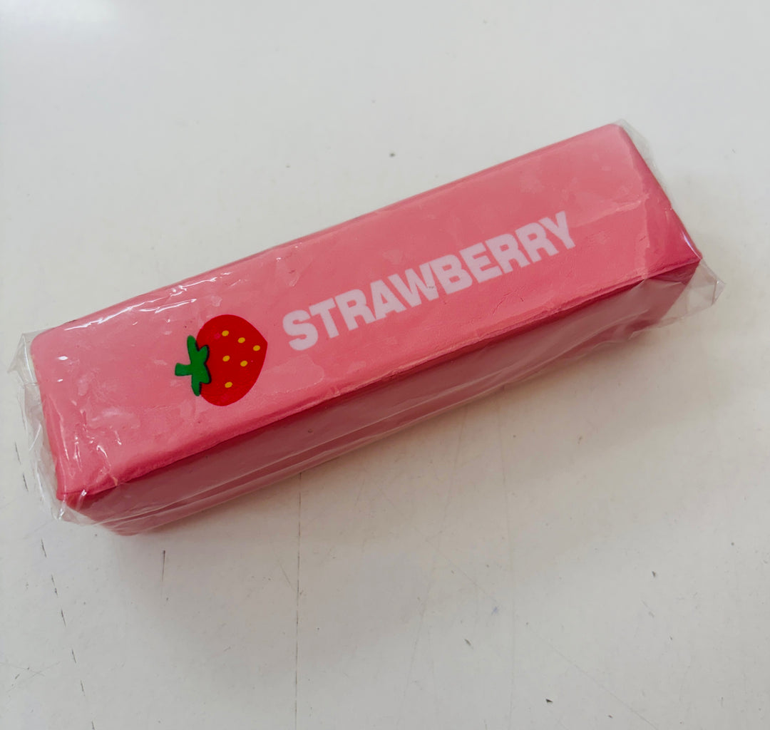 A pink strawberry squishy wrapped in clear plastic, printed with the word 'STRAWBERRY' in white and a small strawberry graphic, placed on a light surface.