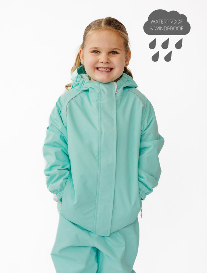 Child wearing a turquoise waterproof jacket and pants on a white background