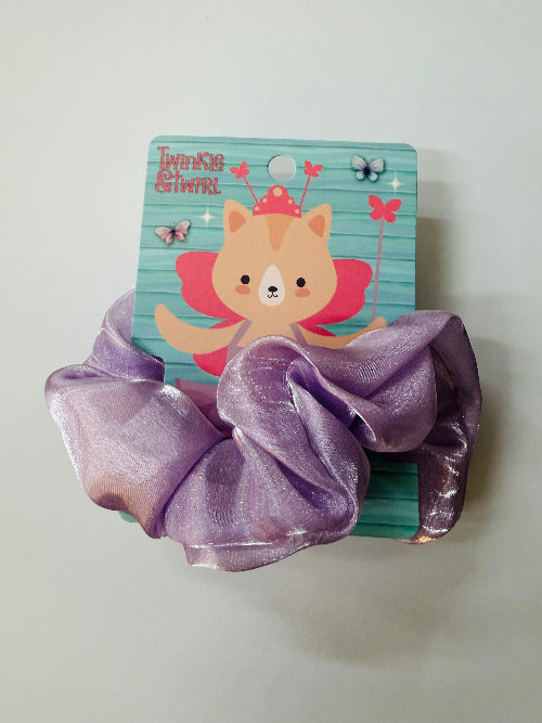 Purple scrunchie on a white surface with a fairy-themed notebook in the background