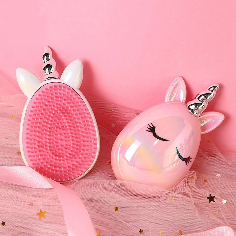 Two unicorn-shaped handheld cleansing brushes on a pink background with tulle and star decorations. One brush is shown from the back with pink bristles, white horn, and white ears; the other is shown from the front in glossy iridescent pink with closed-eye detail and a silver horn.
