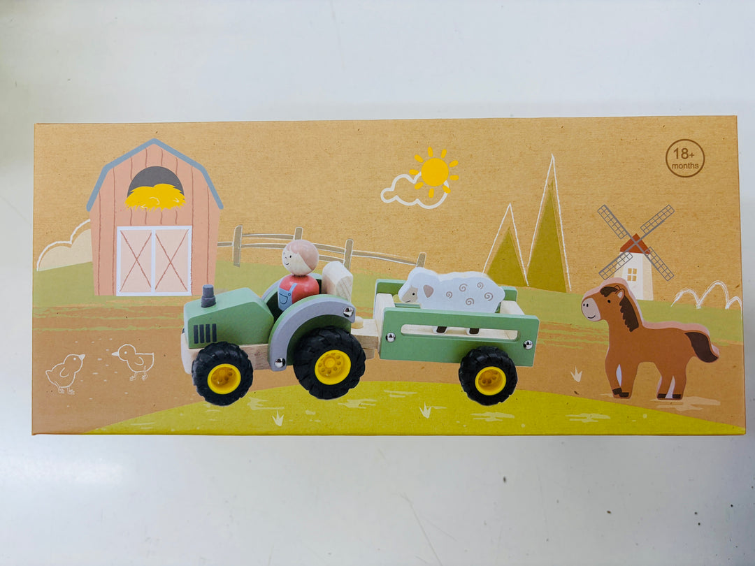 A wooden toy set depicting a farm scene, featuring a green tractor with a trailer carrying a white sheep, alongside a brown horse, barn, windmill, and sun, all printed on a tan cardboard backing.