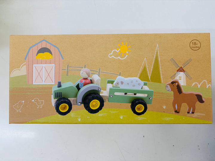 A wooden toy set depicting a farm scene, featuring a green tractor with a trailer carrying a white sheep, alongside a brown horse, barn, windmill, and sun, all printed on a tan cardboard backing.