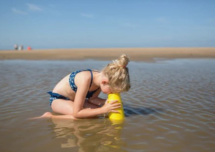 Child playing with a yellow aquascope in shallow water at the beach