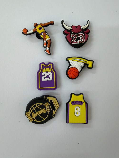 Six basketball-themed shoe charms arranged on a plain white surface, featuring Kobe Bryant, LeBron James, and Kyrie Irving designs in purple, yellow, black, and orange.