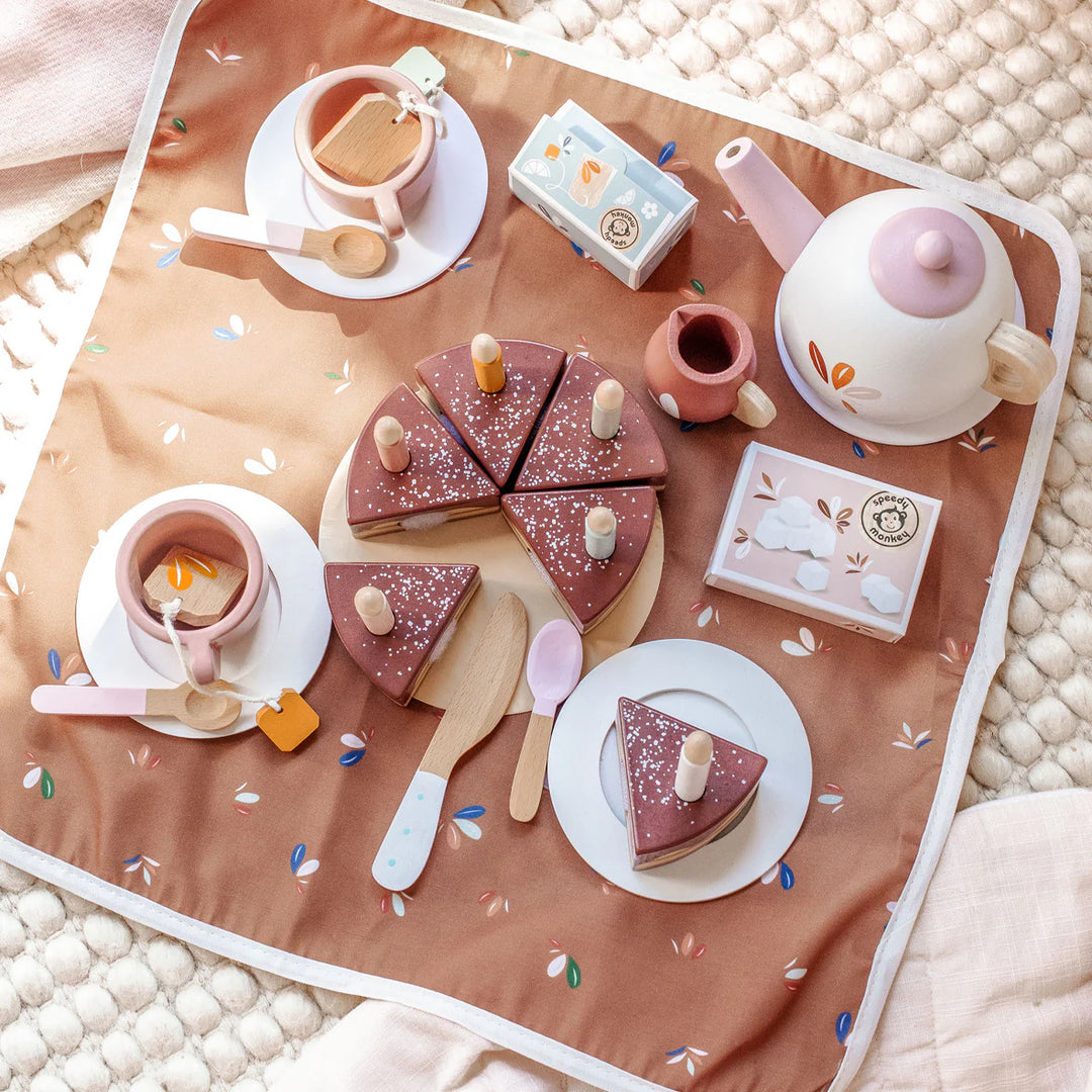 Tea set and cake slices on a decorative blanket with floral patterns.