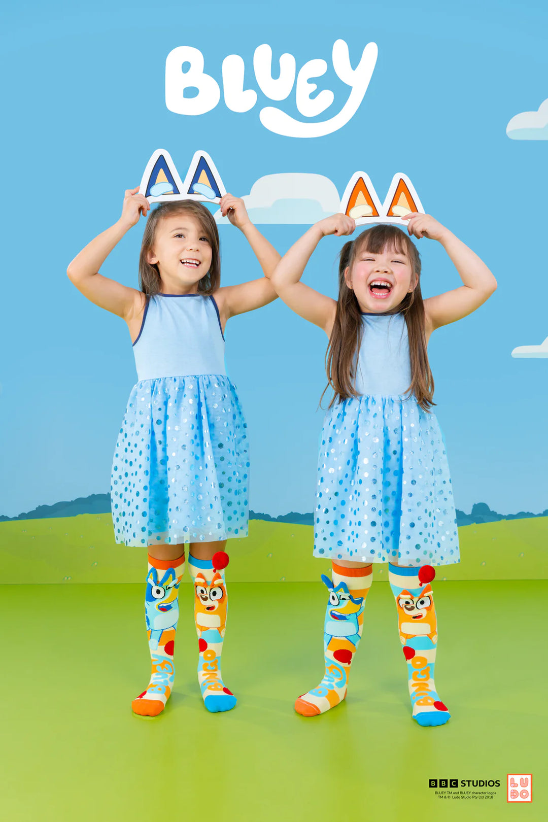 Two children in matching outfits with cartoon character socks, holding cat ears against a blue sky.