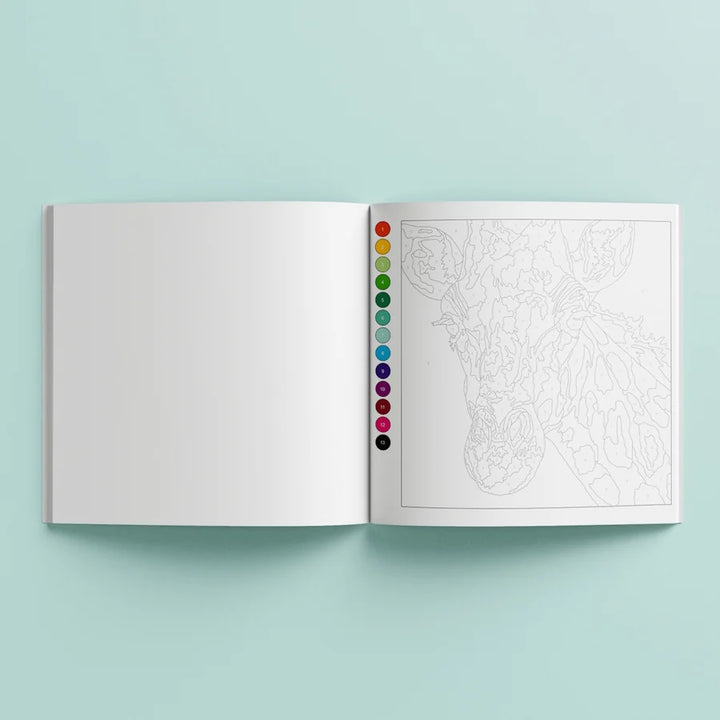 An open coloring book or art booklet on a light mint background. The left page is blank white, and the right page shows a lightly sketched line drawing with a vertical row of colored circular swatches along the center edge.