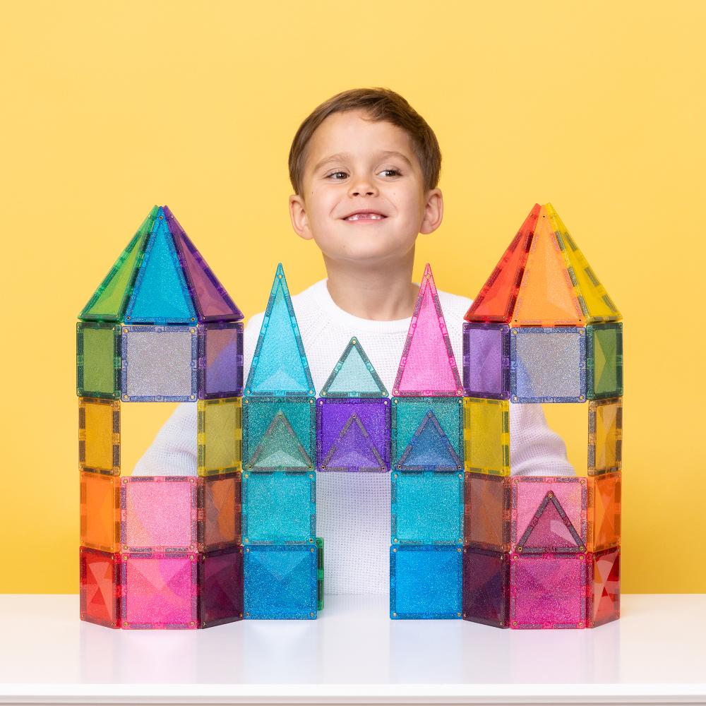Child with colorful connetix magnetic building blocks shaped like a castle on a yellow background