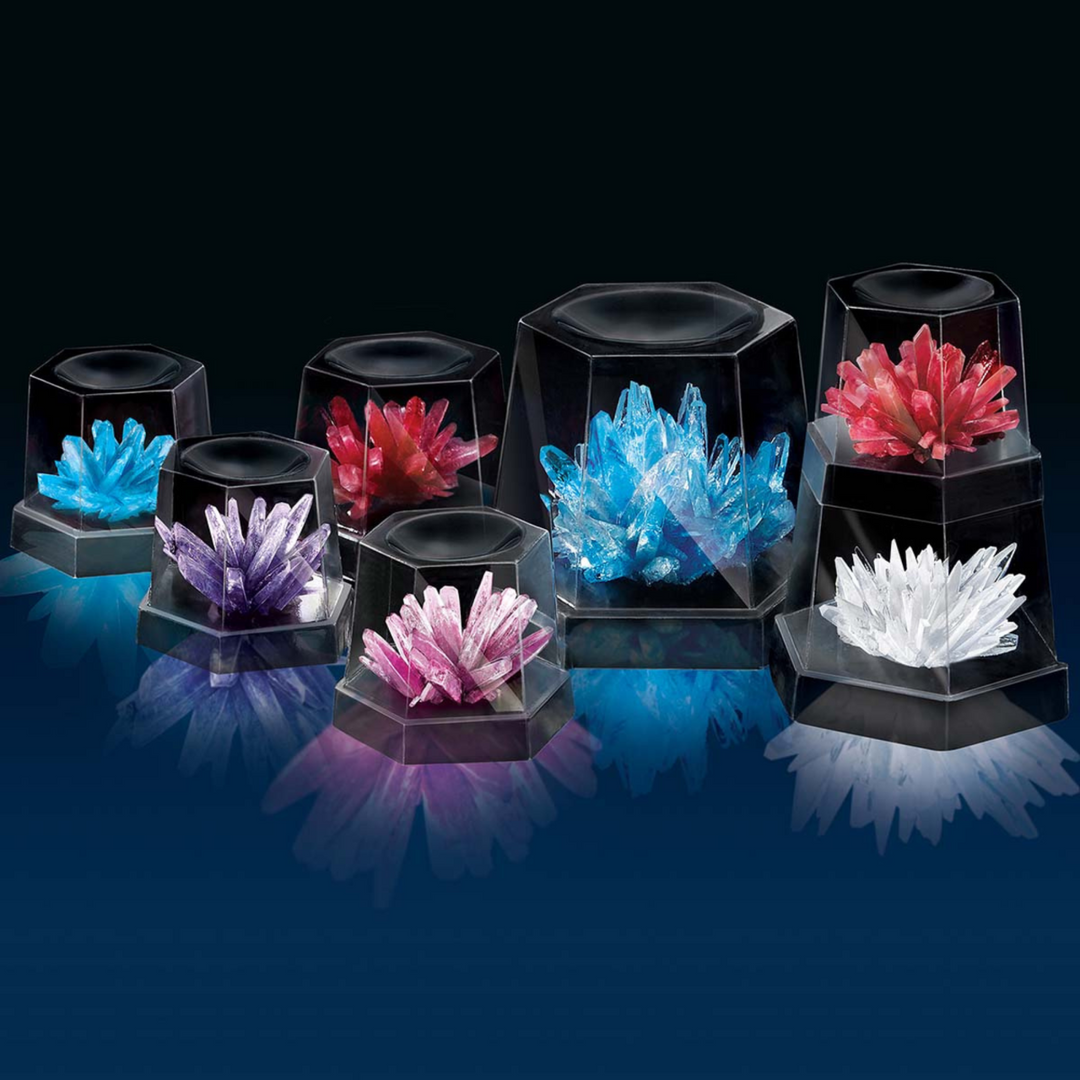 A set of eight black hexagonal crystal display boxes arranged on a dark reflective surface, each holding a different colored crystal cluster including blue, red, purple, pink, and white.