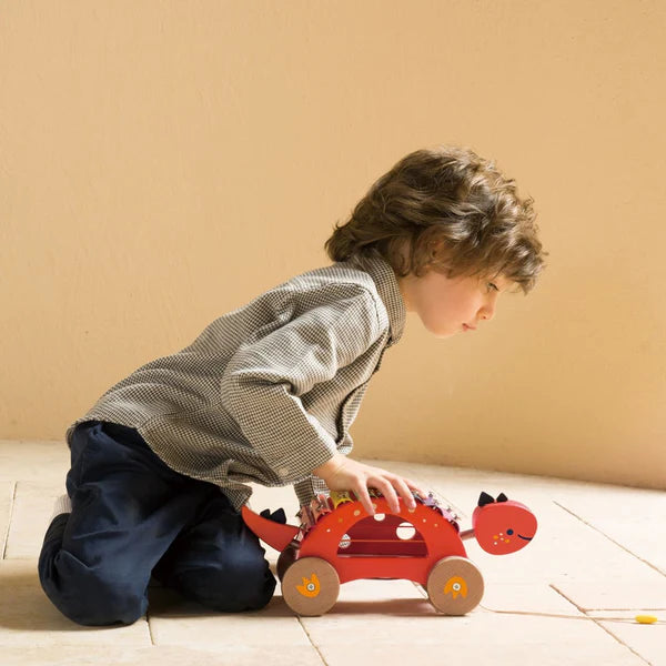 Child playing with a red toy car on a wooden floor.