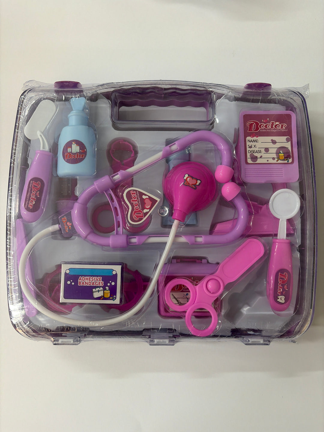 Toy medical set with pink stethoscope and other tools in a clear case on a white background