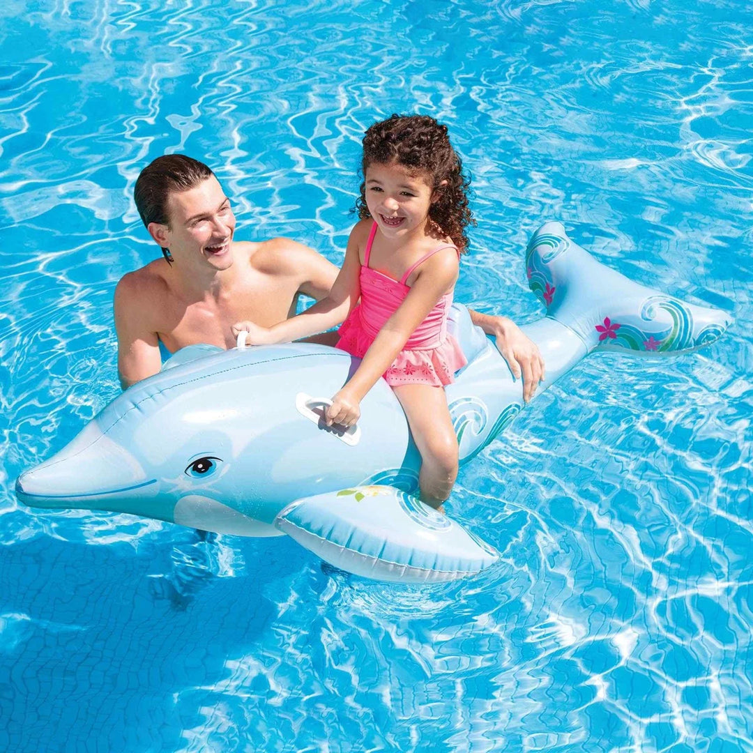 child using dolphin ride on in blue pool whilst man stands next to her 