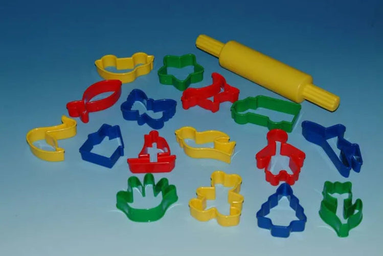 A set of colorful plastic cookie cutters and a yellow rolling pin arranged on a blue gradient background. The cutters are in red, green, blue, and yellow, and include various shapes like a fish, house, boat, tree, and flower.