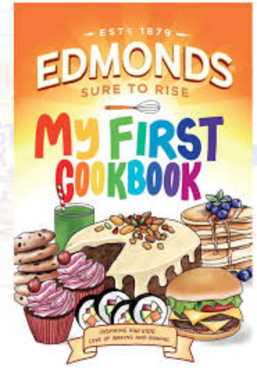 Front cover of the children's book 'Edmonds Sure to Rise: My First Cookbook' featuring a bright orange and yellow gradient background, colorful title text, and cartoon illustrations of breakfast foods including pancakes, a cake, a cupcake, a burger, and a coffee cup.