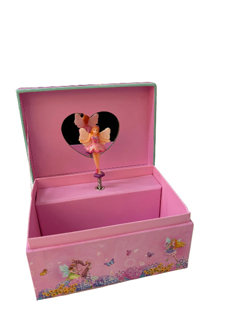 A pink fairy-themed music box with an open lid showing a heart-shaped cutout and a small fairy figure inside, set on a white tabletop with a toy store background.