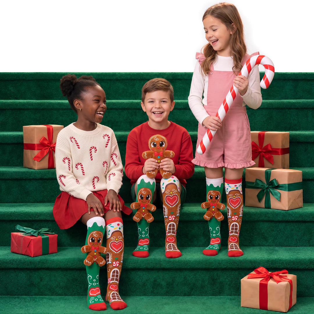 3 children sitting on green staircase wearing gingerbread socks with presents around them for decoration