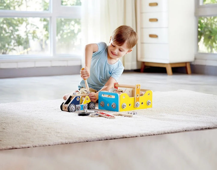 Child playing with a toy truck set on a carpeted floor. Hape Build It Tool Box