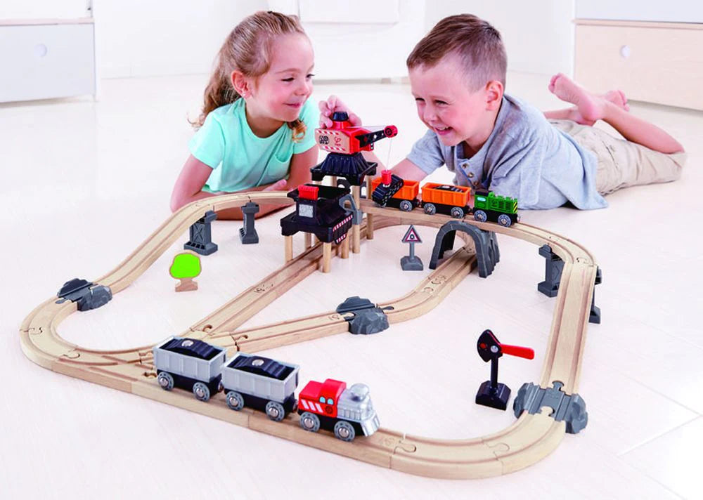 Two children playing with a hape mining loader train set on a white floor.