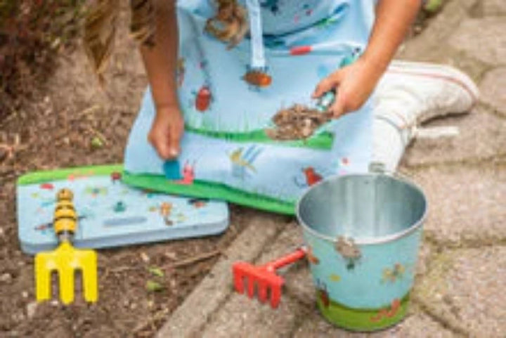 Child in a gardening apron with tools and a bucket on a garden path