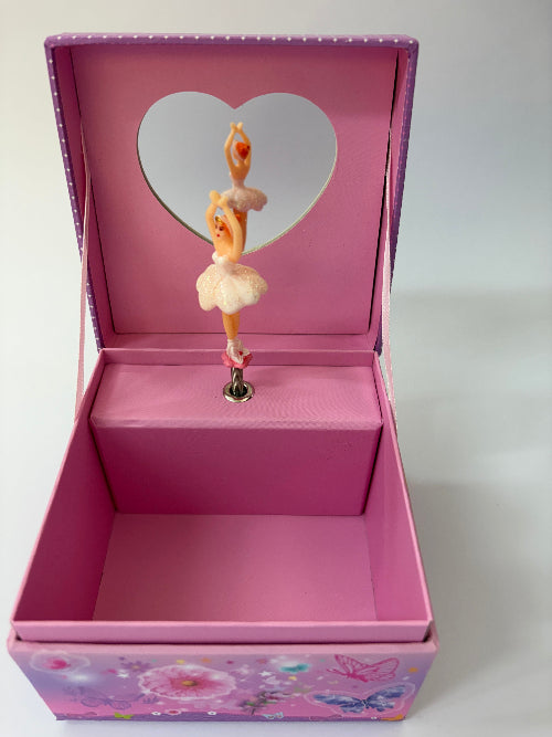 A pink music box jewelry box with a ballerina figurine standing in the center. The lid is open, showing a heart-shaped mirror on the inner lid and a floral pattern on the front.