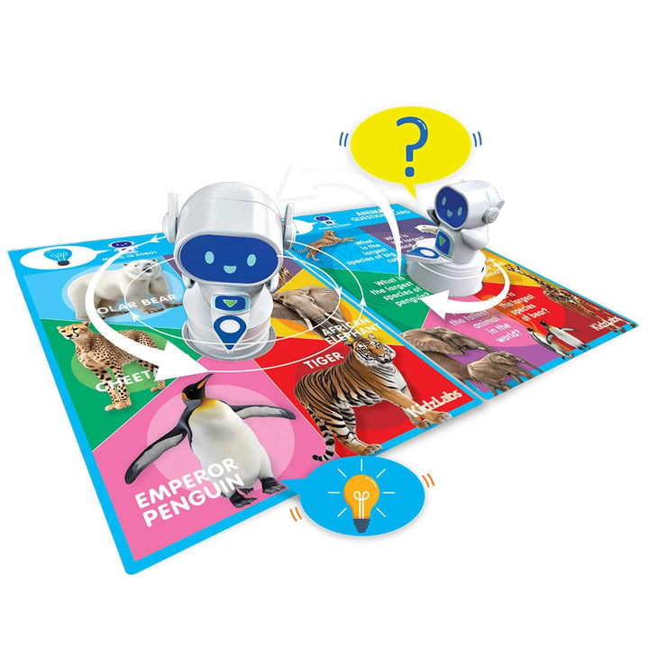 A children's educational toy set featuring two white robot figures with blue visors placed on a colorful animal-themed game mat. The mat shows animal illustrations and text such as 'Emperor Penguin' and 'Tiger,' with a yellow speech bubble containing a question mark above one robot and a blue light-bulb icon below.